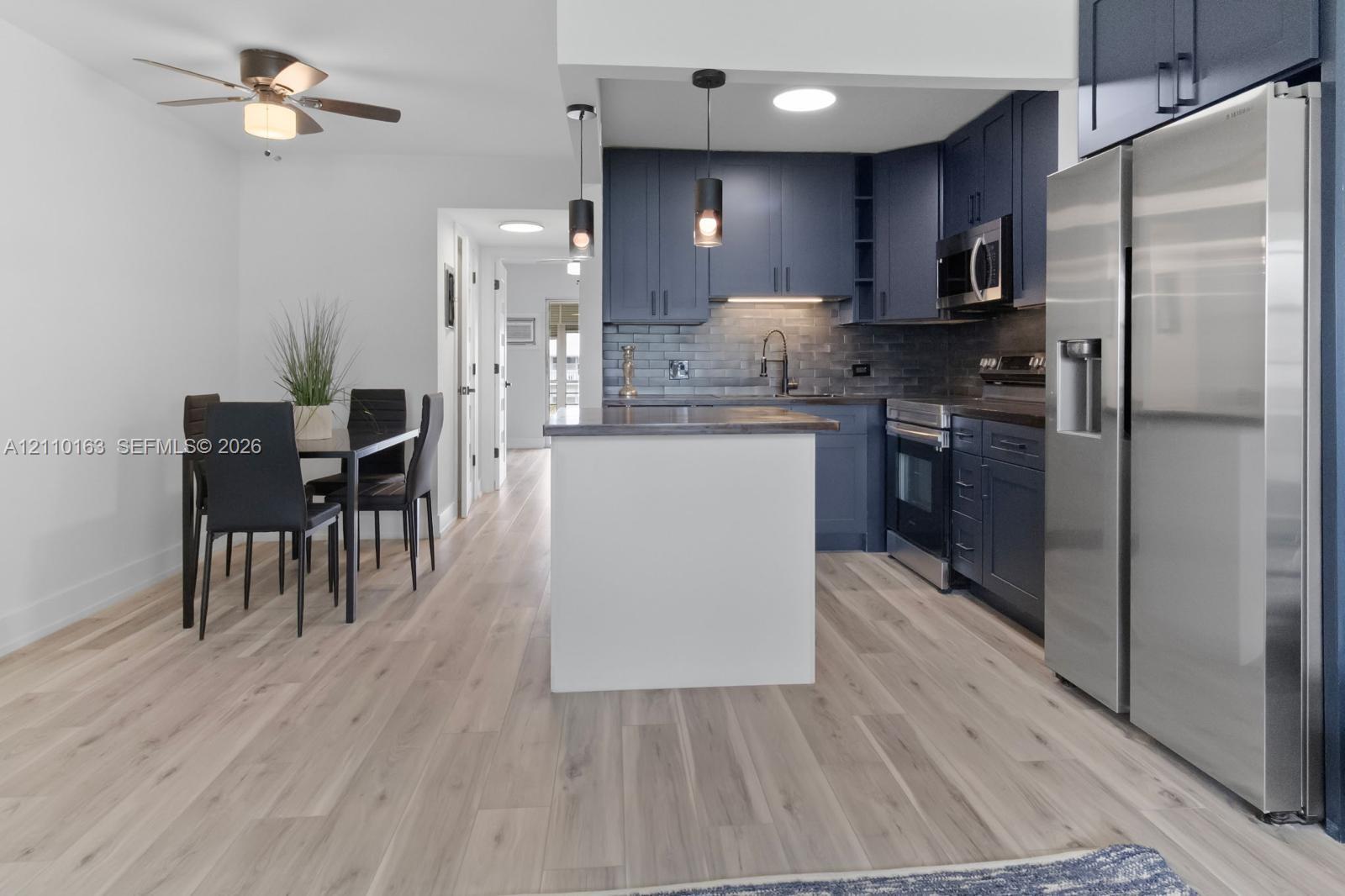Kitchen featuring dark cabinetry, stainless steel appliances, a white kitchen island, pendant lighting, and wood-finish flooring