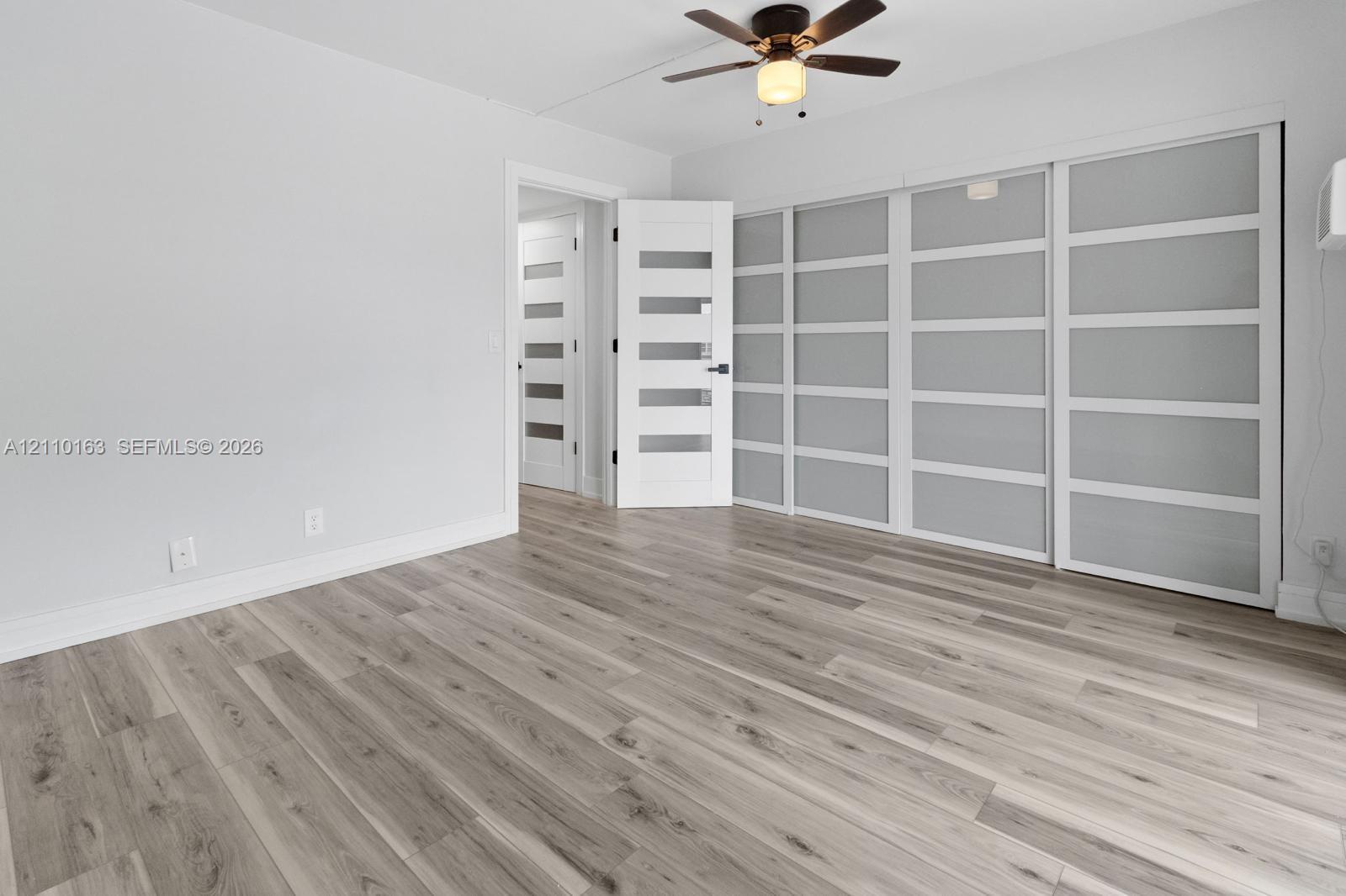 Wood-finish flooring, multi-panel sliding closet doors with frosted glass inserts, five-panel interior doors, and a ceiling fan with integrated lighting