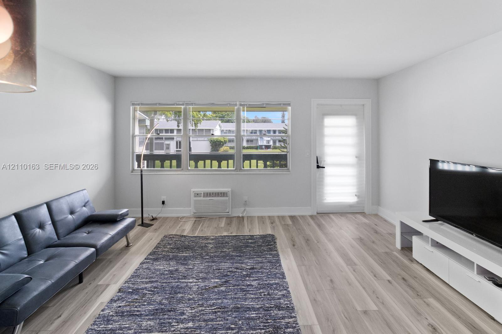 Neutral-toned interior featuring wood-finish flooring, a triple-pane window configuration, and an exterior entry door with integrated blind