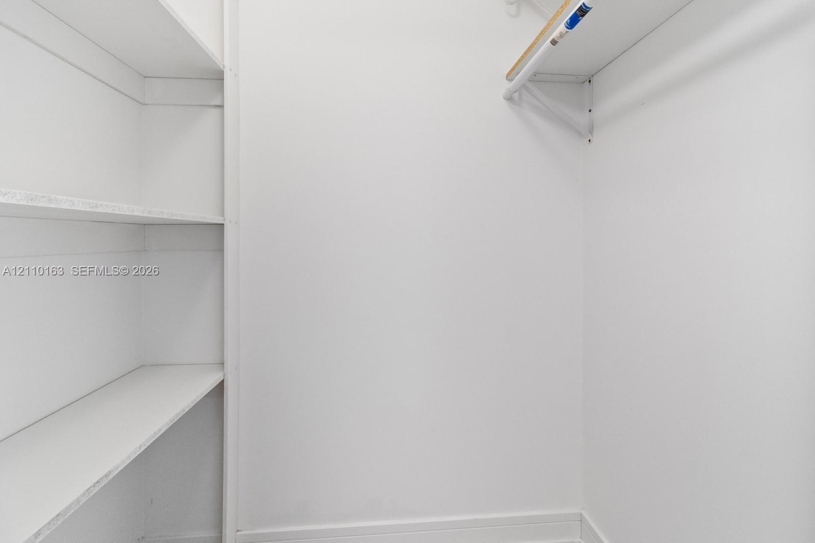 Built-in white shelving unit featuring four storage levels, complemented by a white hanging rod and overhead shelf