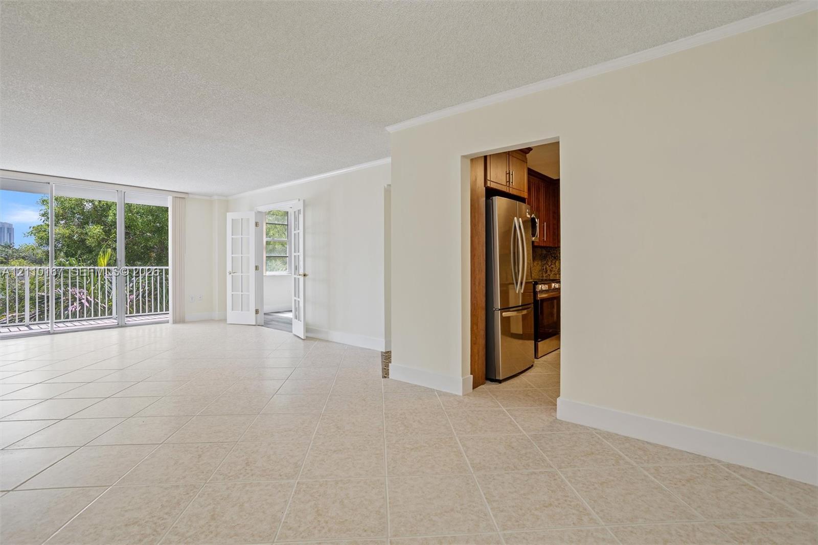 Spacious room featuring neutral tile flooring, floor-to-ceiling glass paneling, French doors, and stainless steel kitchen appliances Spacious room featuring neutral tile flooring, floor-to-ceiling glass paneling, French doors, and stainless steel kitchen appliances