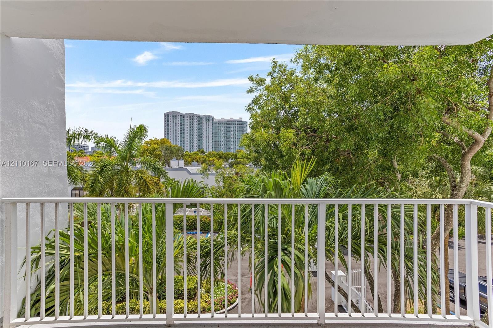 Private balcony featuring a white metal railing, mature palm trees, and exterior foliage Private balcony featuring a white metal railing, mature palm trees, and exterior foliage