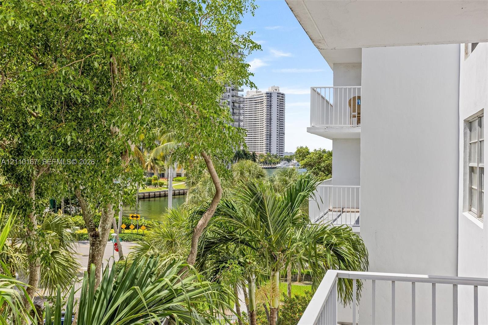 Private balcony with white metal railings, overlooking lush landscaping, mature trees, and a canal Private balcony with white metal railings, overlooking lush landscaping, mature trees, and a canal