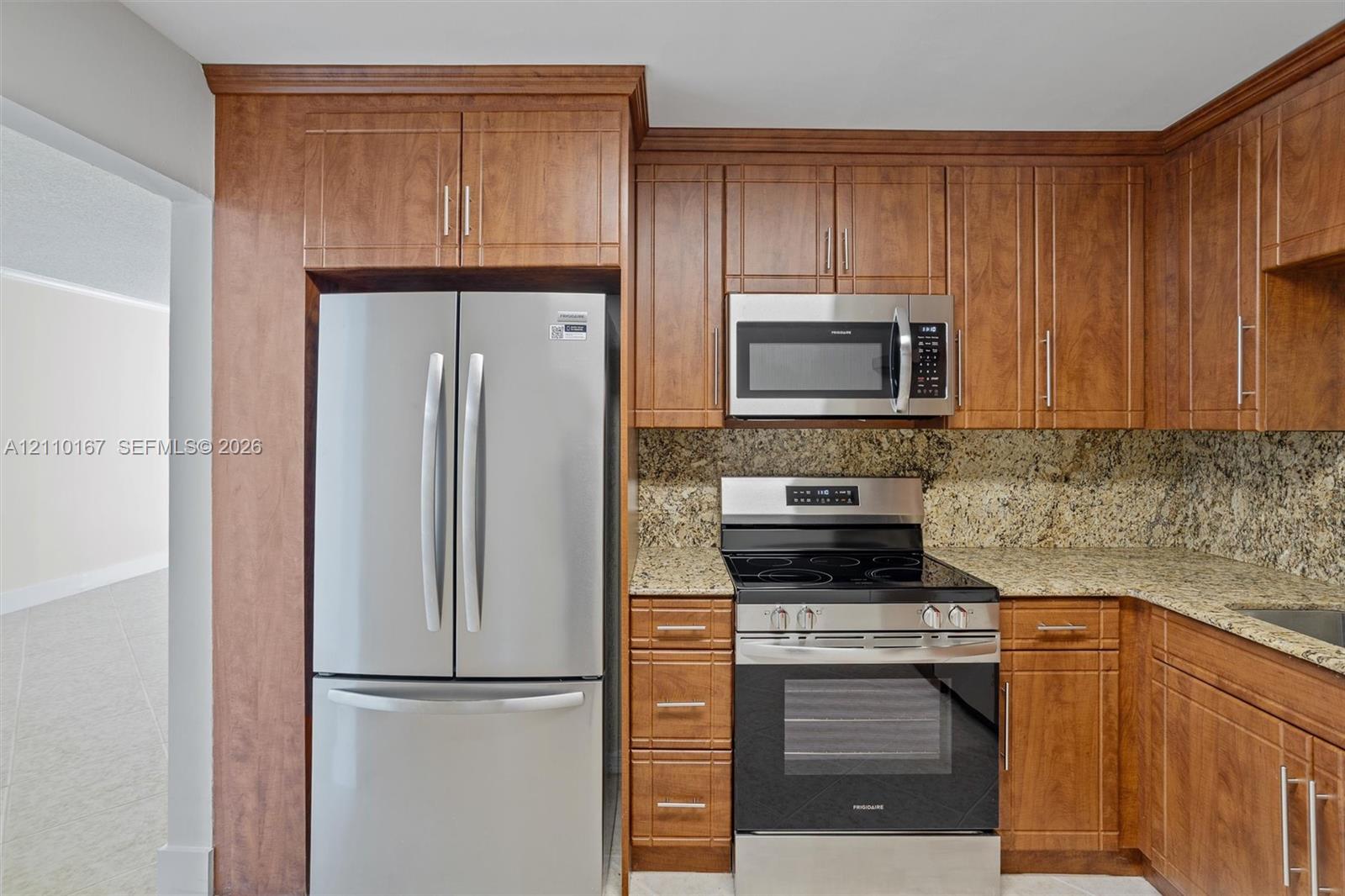 Kitchen featuring wood cabinetry, stone countertops, stone tile backsplash, and stainless steel appliances including a French door refrigerator, over-the-range microwave, and a slide-in range Kitchen featuring wood cabinetry, stone countertops, stone tile backsplash, and stainless steel appliances including a French door refrigerator, over-the-range microwave, and a slide-in range