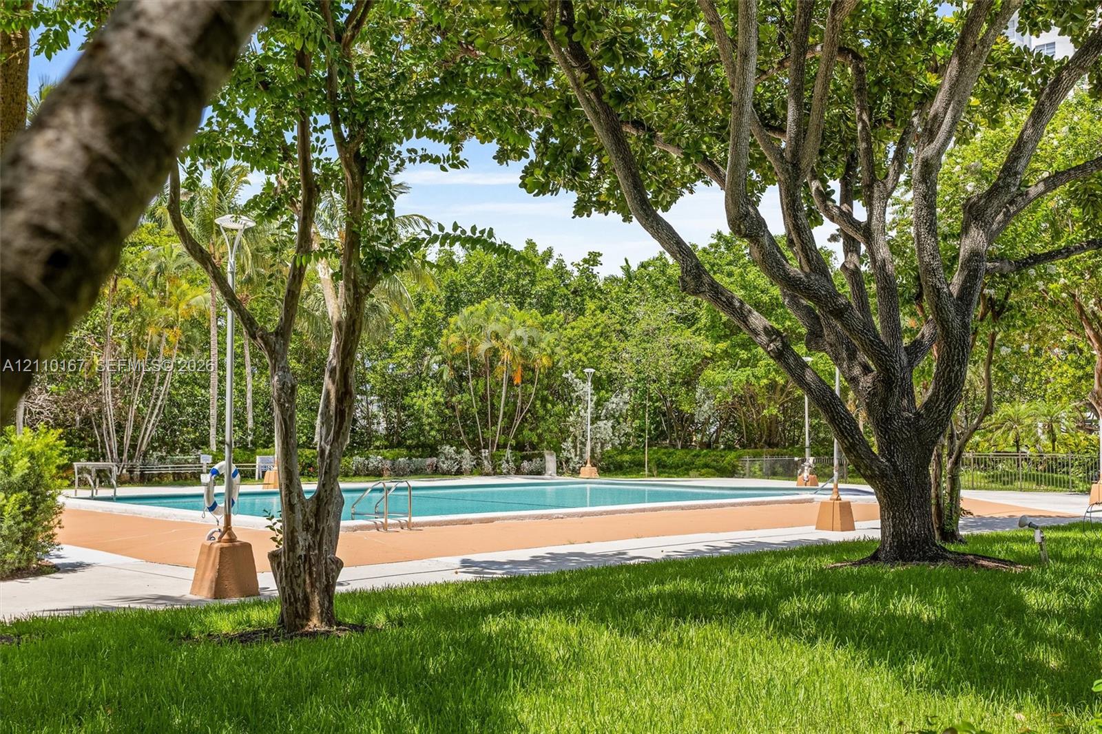 Swimming pool with a solid-surface deck, surrounded by mature trees, landscaping, and integrated lighting fixtures
