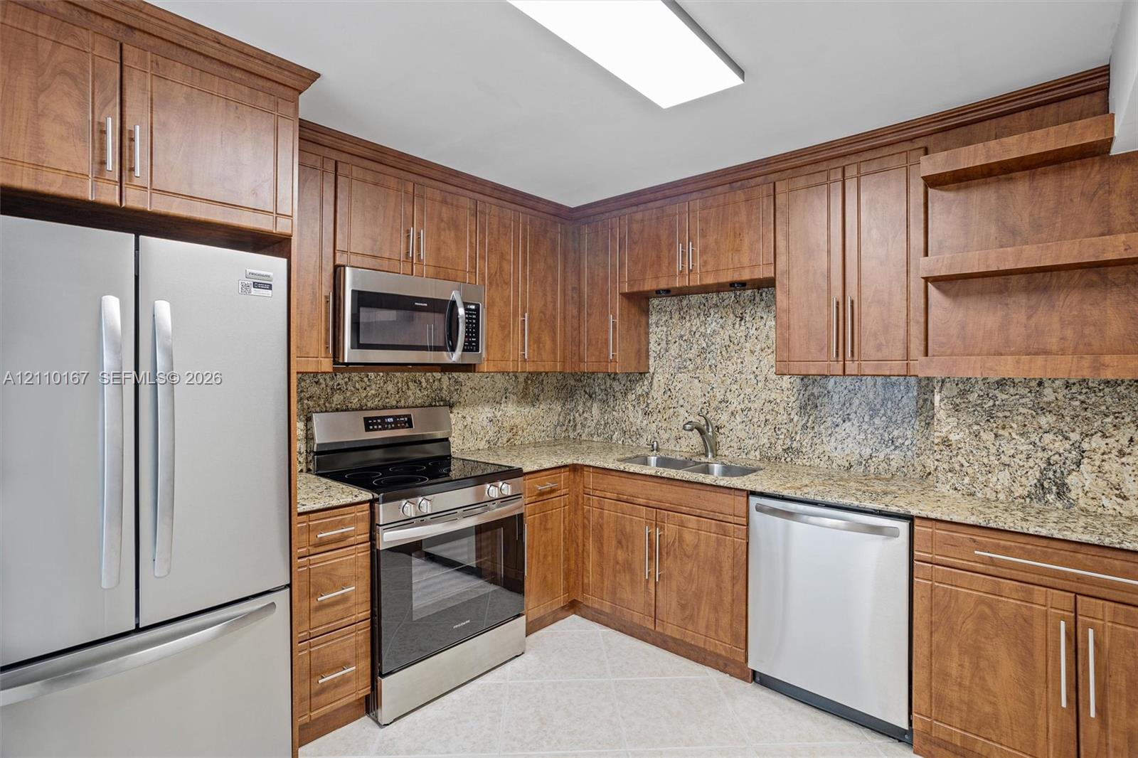 Kitchen featuring wood cabinetry, stone countertops, stone tile backsplash, stainless steel appliances, and built-in shelving Kitchen featuring wood cabinetry, stone countertops, stone tile backsplash, stainless steel appliances, and built-in shelving