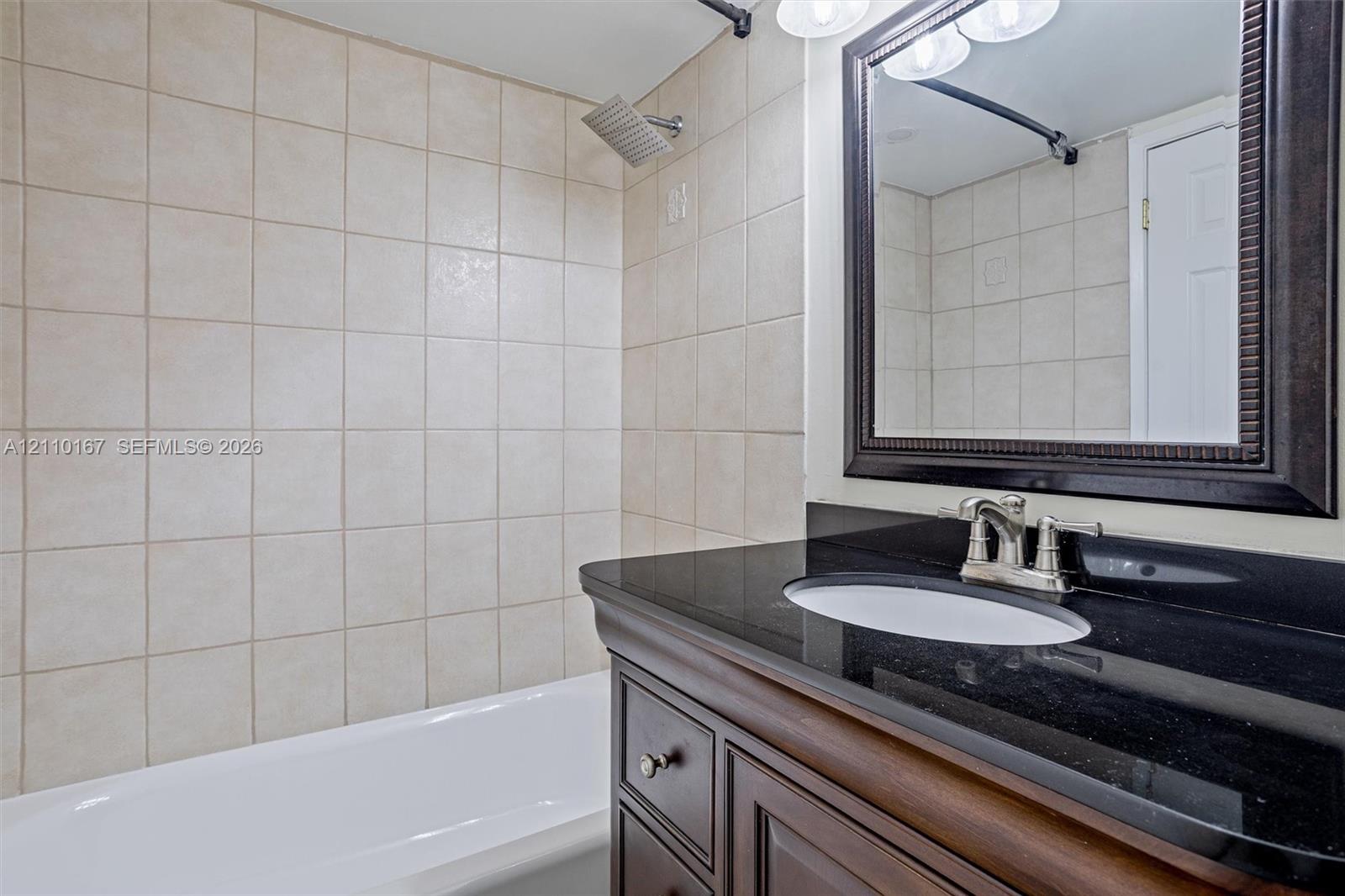 Bathroom vanity featuring a dark stone countertop, an integrated oval sink, and wood-finish cabinetry, complemented by a tile-surround bathtub and a framed wall mirror