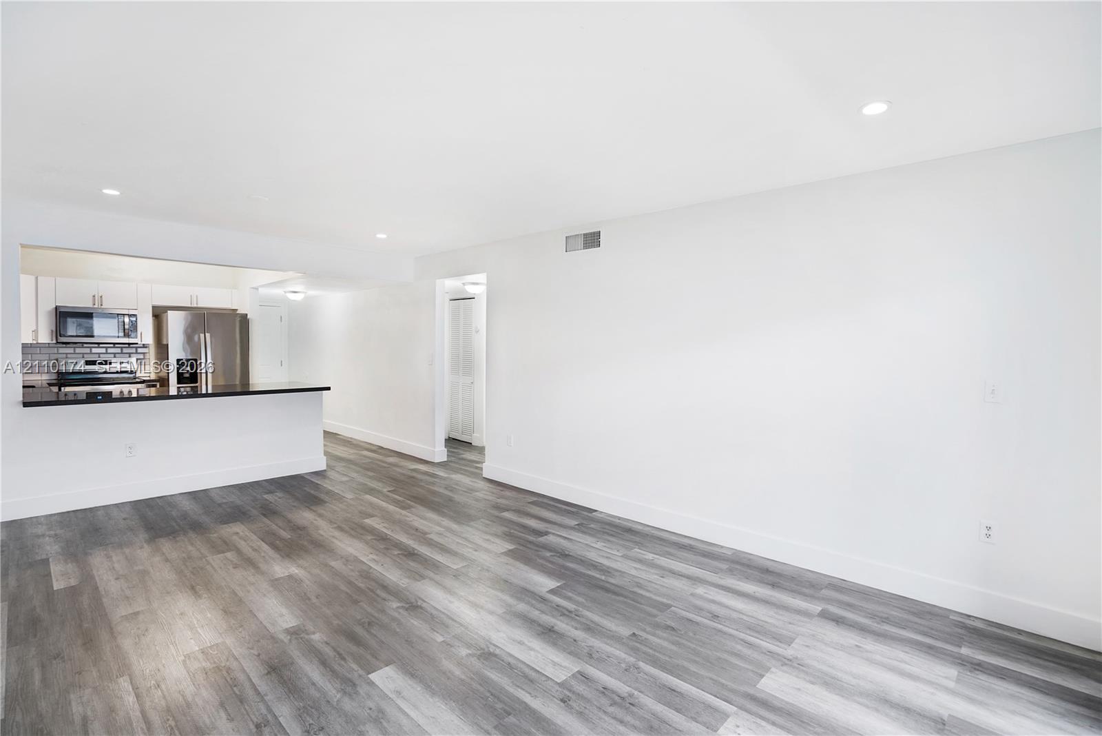 Open-concept interior featuring wood-finish flooring, recessed lighting, and a kitchen peninsula with a dark countertop and white cabinetry Open-concept interior featuring wood-finish flooring, recessed lighting, and a kitchen peninsula with a dark countertop and white cabinetry