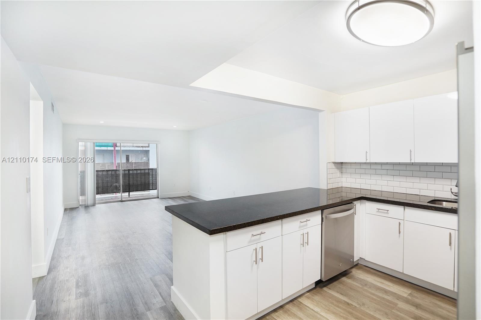 Kitchen featuring white cabinetry, dark countertops, subway tile backsplash, stainless steel dishwasher, and wood-finish flooring Kitchen featuring white cabinetry, dark countertops, subway tile backsplash, stainless steel dishwasher, and wood-finish flooring