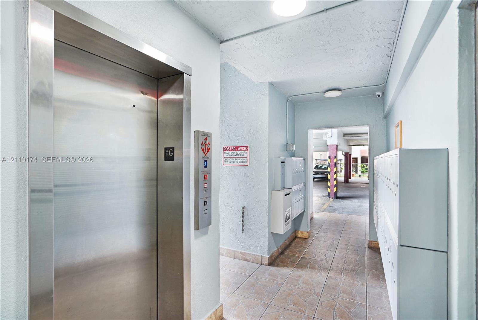 Stainless steel elevator entrance with matching control panel, ceramic tile flooring, and integrated wall-mounted mailboxes