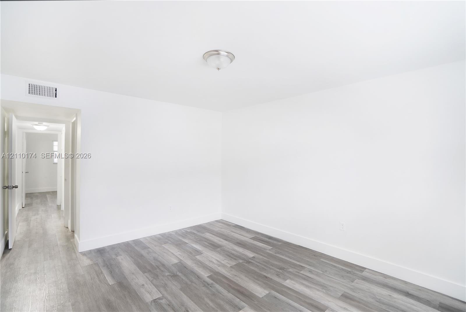 Room interior featuring wood-finish flooring, white walls, and a ceiling-mounted light fixture