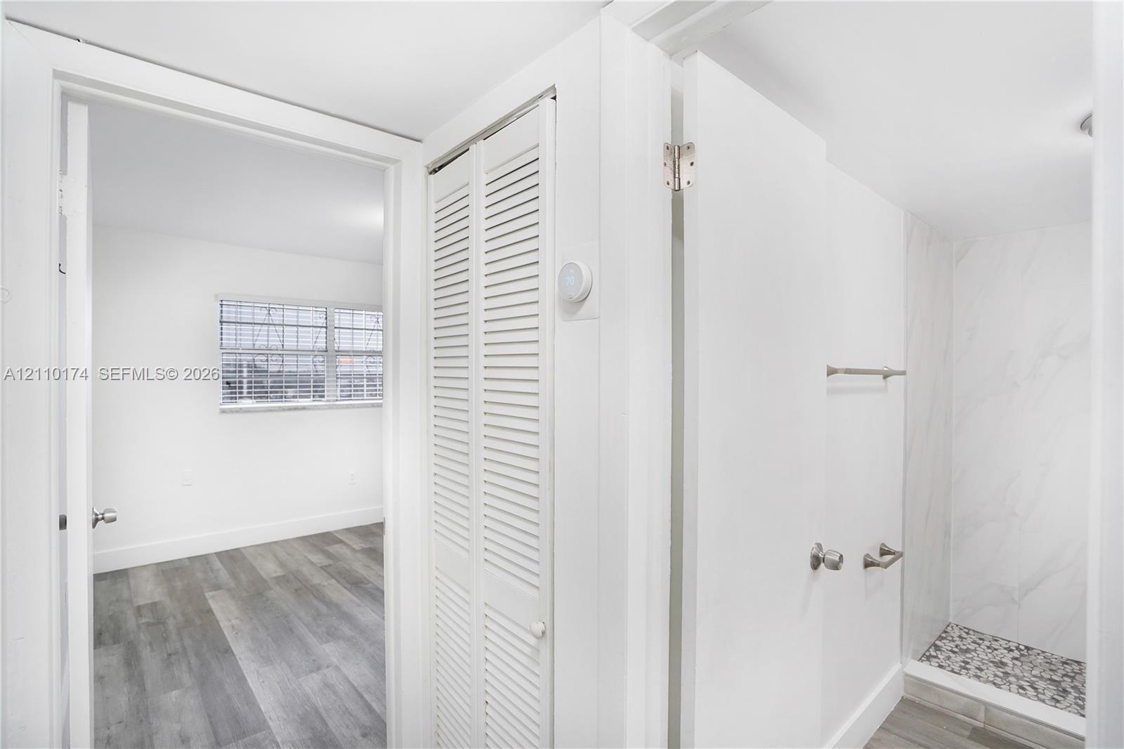 Walk-in shower with stone-finish tile surround and pebble-texture flooring, white louvered closet doors, and wood-finish flooring