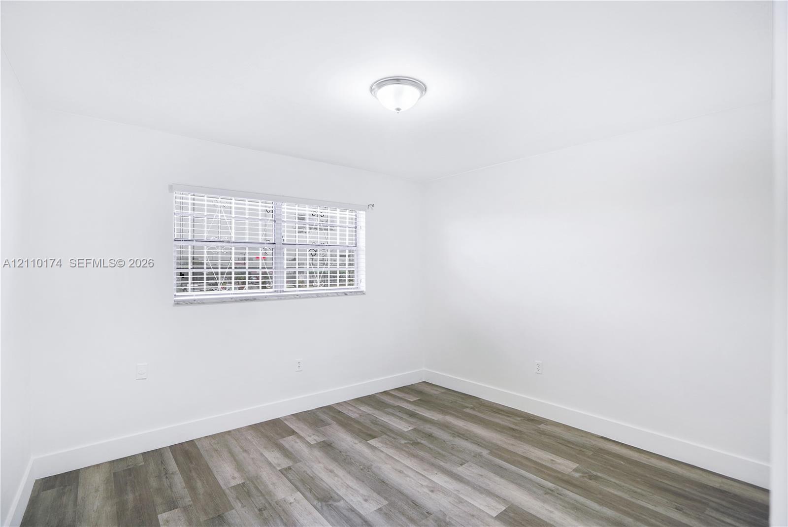 Interior space featuring wood-finish flooring, white walls, a flush-mount ceiling light fixture, and a single window with horizontal blinds