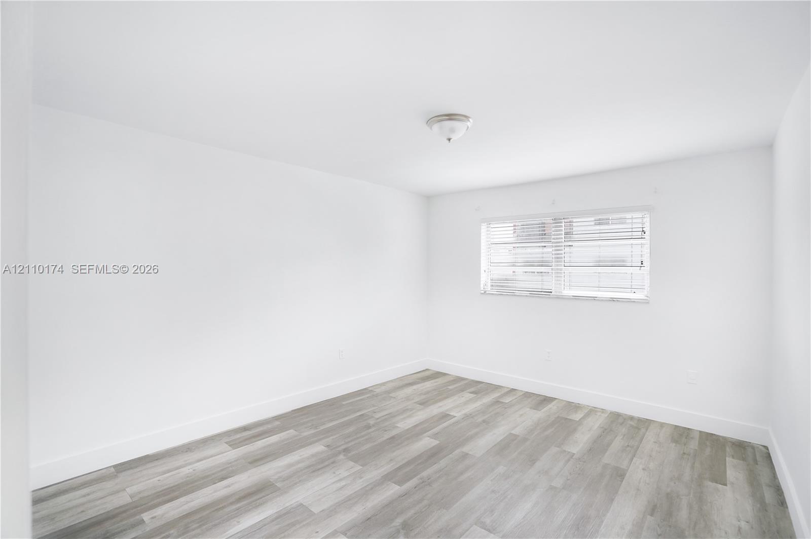 Neutral-toned room featuring wood-finish flooring, white walls, and a center-mount flush light fixture