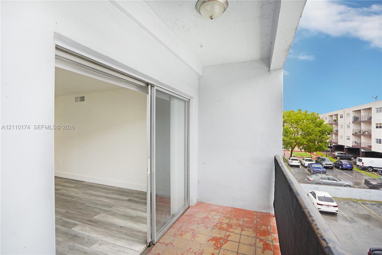 Covered balcony featuring tile flooring, metal railing, and ceiling-mounted light fixture, accessed via sliding glass doors