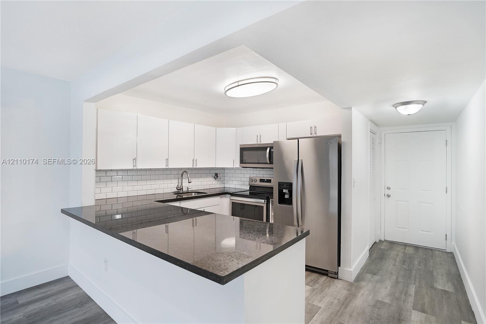 Kitchen featuring white cabinetry, dark stone countertops, stainless steel appliances, a white subway tile backsplash, and wood-finish flooring Kitchen featuring white cabinetry, dark stone countertops, stainless steel appliances, a white subway tile backsplash, and wood-finish flooring