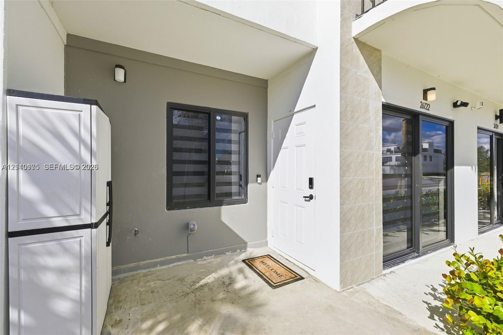 Covered entryway featuring a concrete porch, neutral-toned exterior walls, modern dark-framed windows, a multi-panel entry door, and wall-mounted exterior lighting