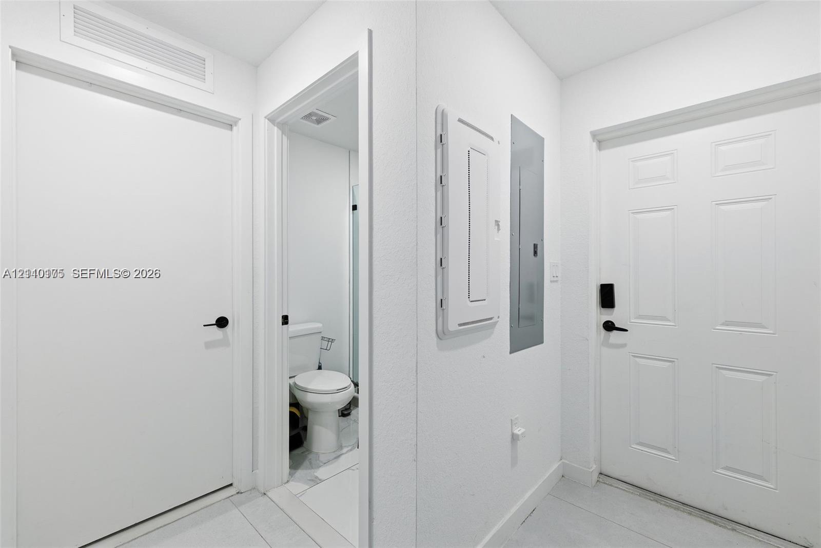 Interior hallway featuring paneled doors with matte black hardware, ceramic tile flooring, and integrated electrical service panel