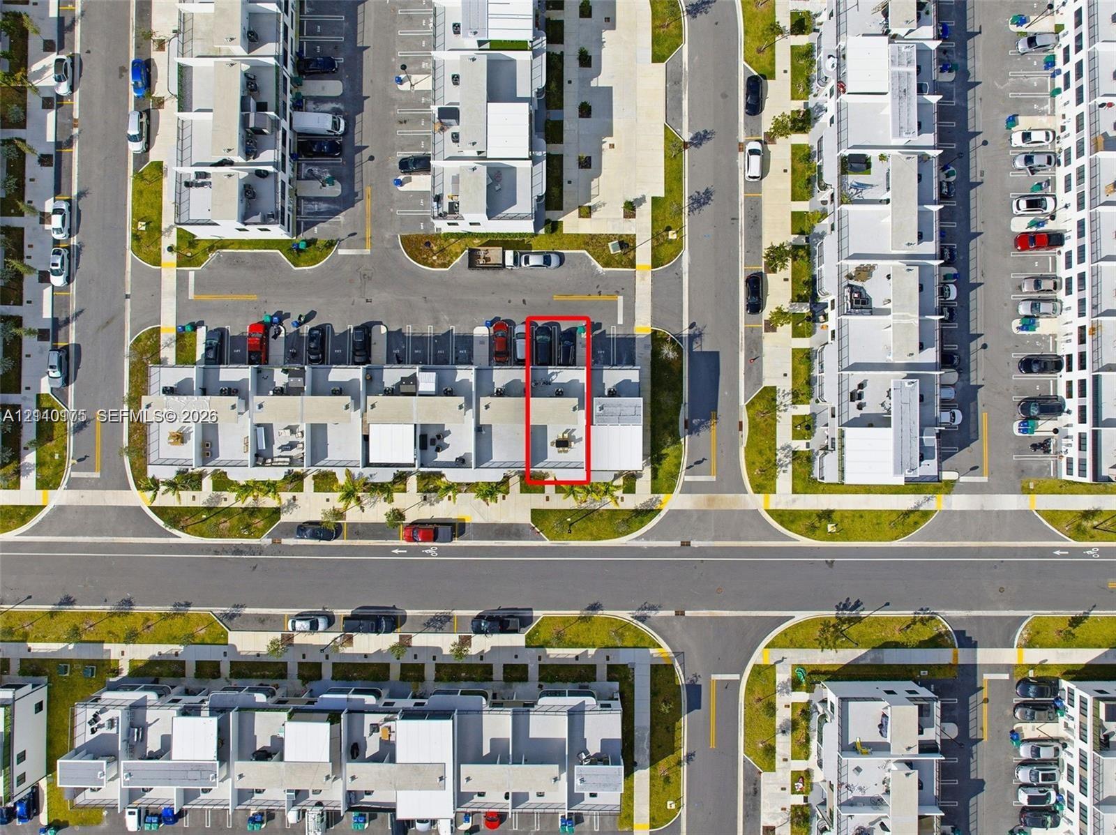 Aerial view of a residential unit featuring a paved rear patio, designated parking spaces, and proximity to internal roadways within the community
