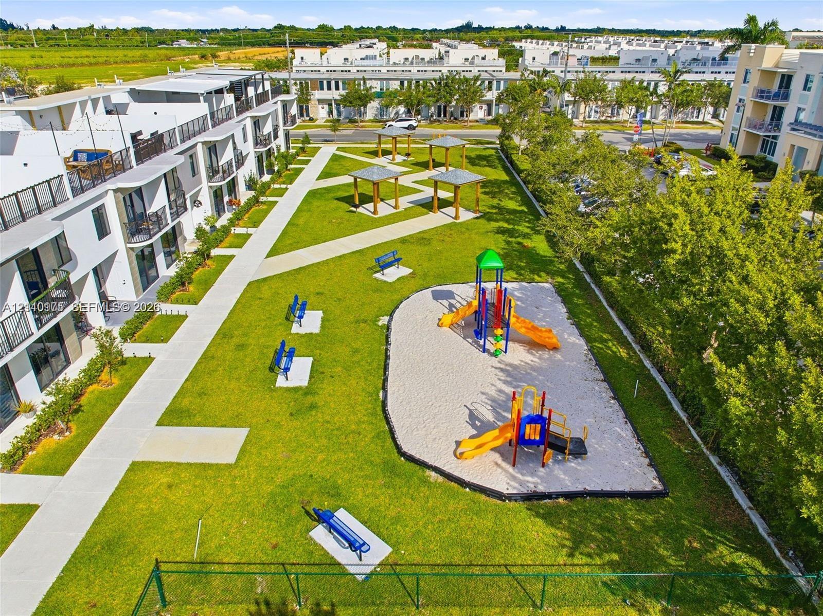 Community grounds featuring a playground, multiple shaded pergolas, concrete walking paths, and expansive green space