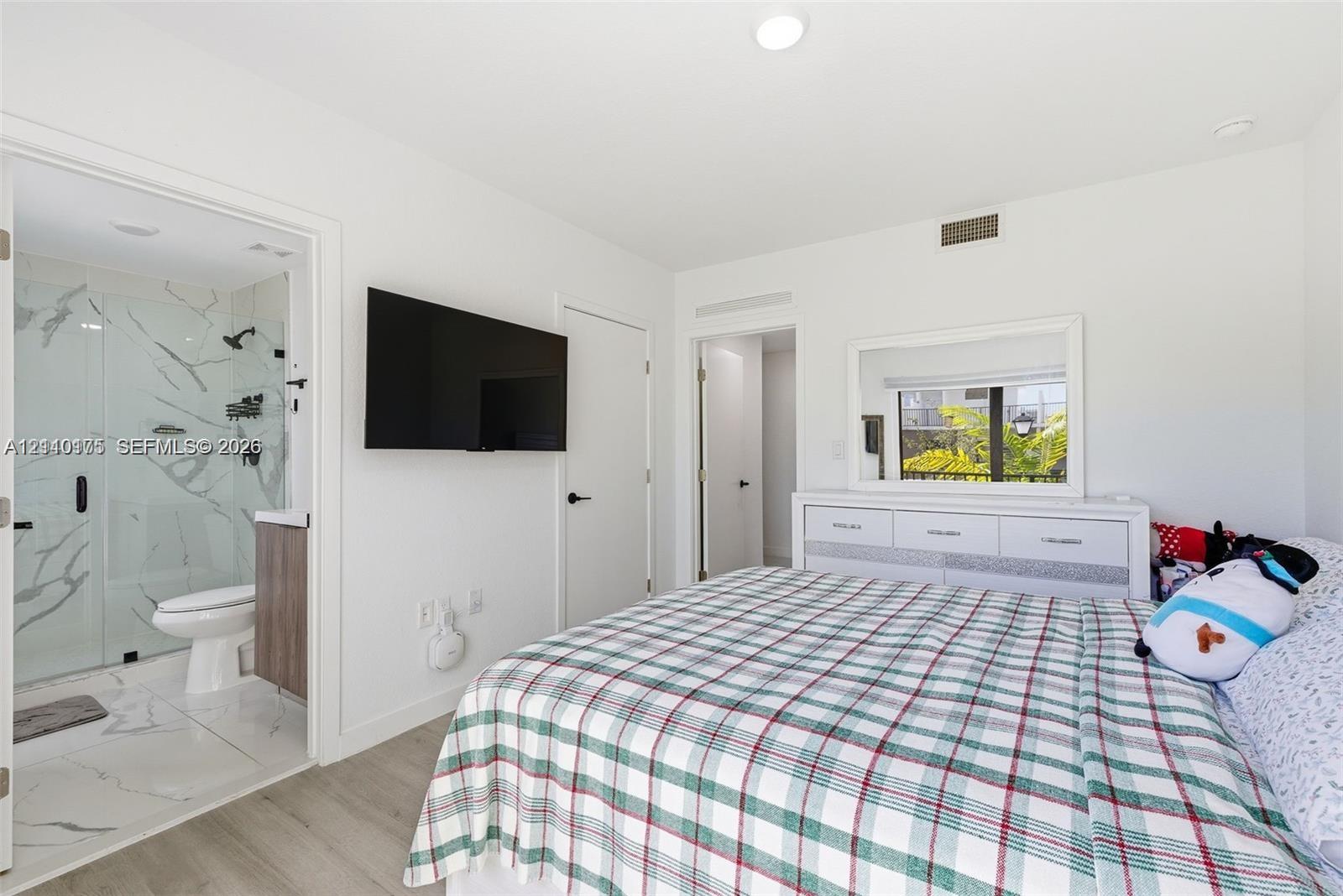 Bedroom featuring wood-finish flooring, recessed lighting, and a private bath with a glass-enclosed shower featuring large-format veined tile and a floating vanity