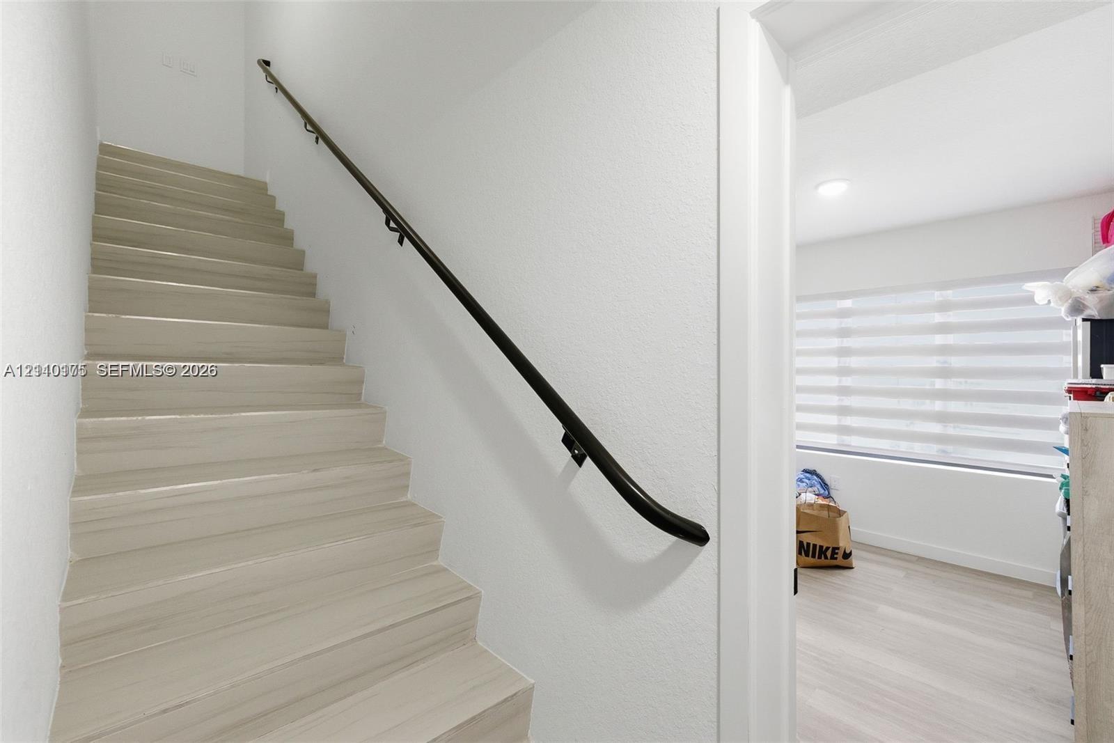 Staircase featuring light wood-finish treads and a matte black wall-mounted handrail