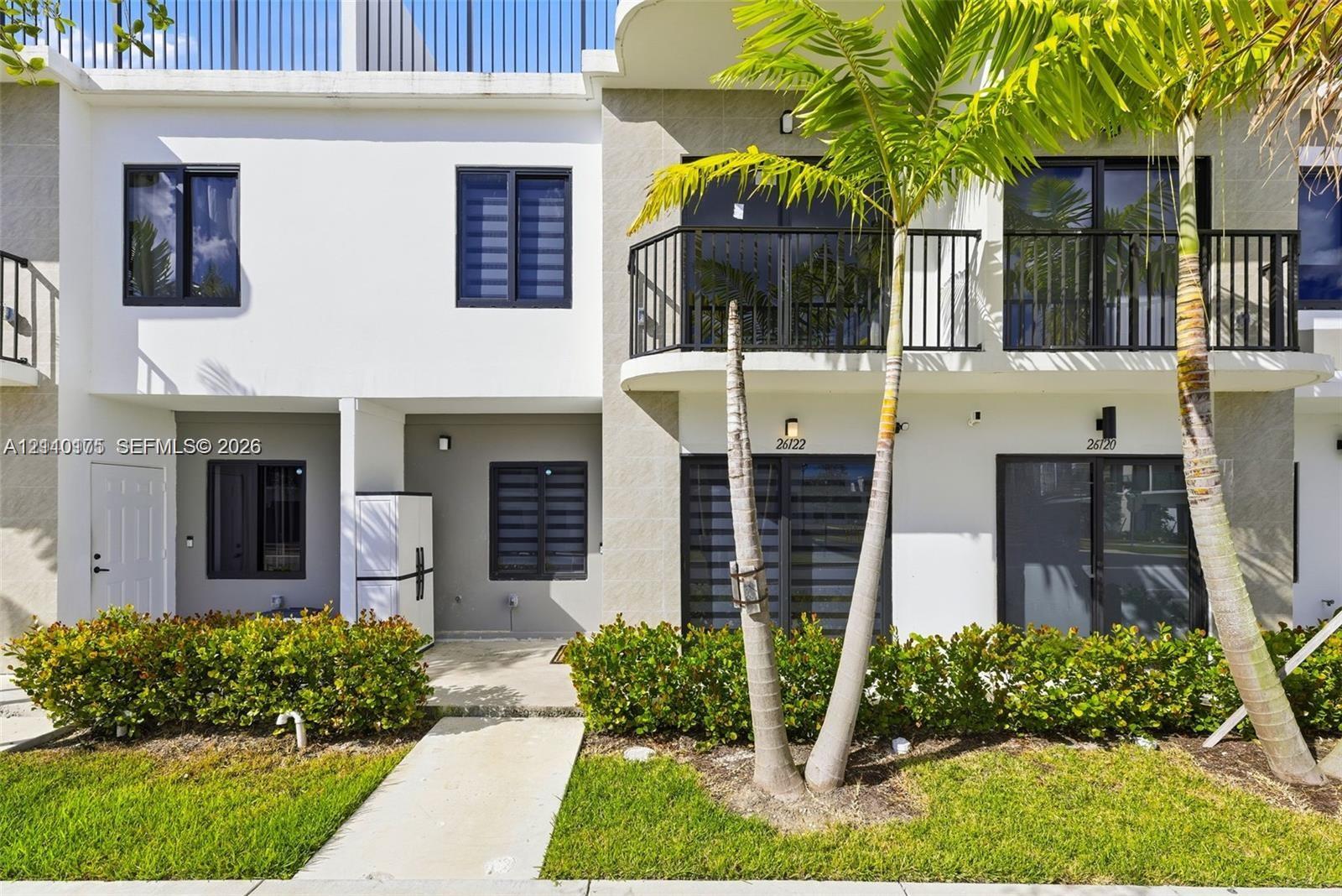Two-story townhome exterior featuring a private second-level balcony with black metal railings, smooth stucco finish, dark-framed multi-pane windows, and integrated wall-mounted exterior lighting