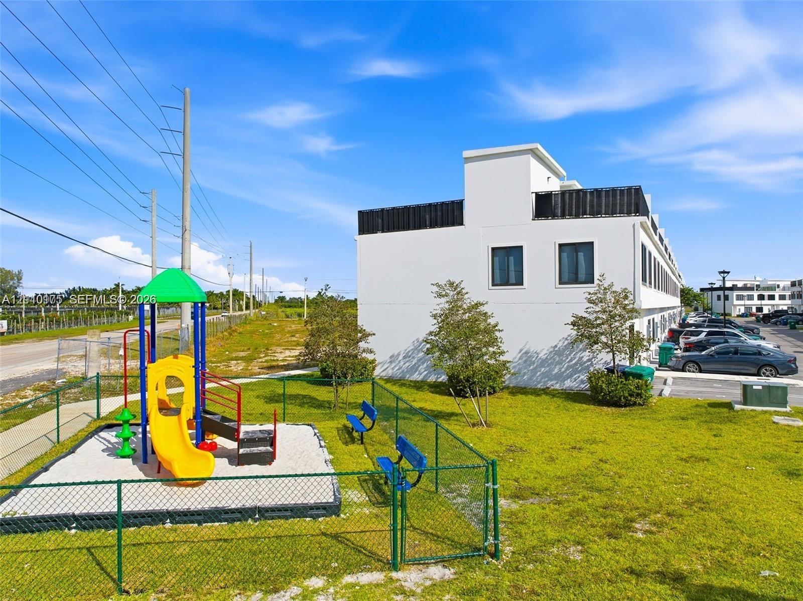 Exterior grounds featuring a fenced-in playground area with a slide and climbing structure, green space, and surface parking