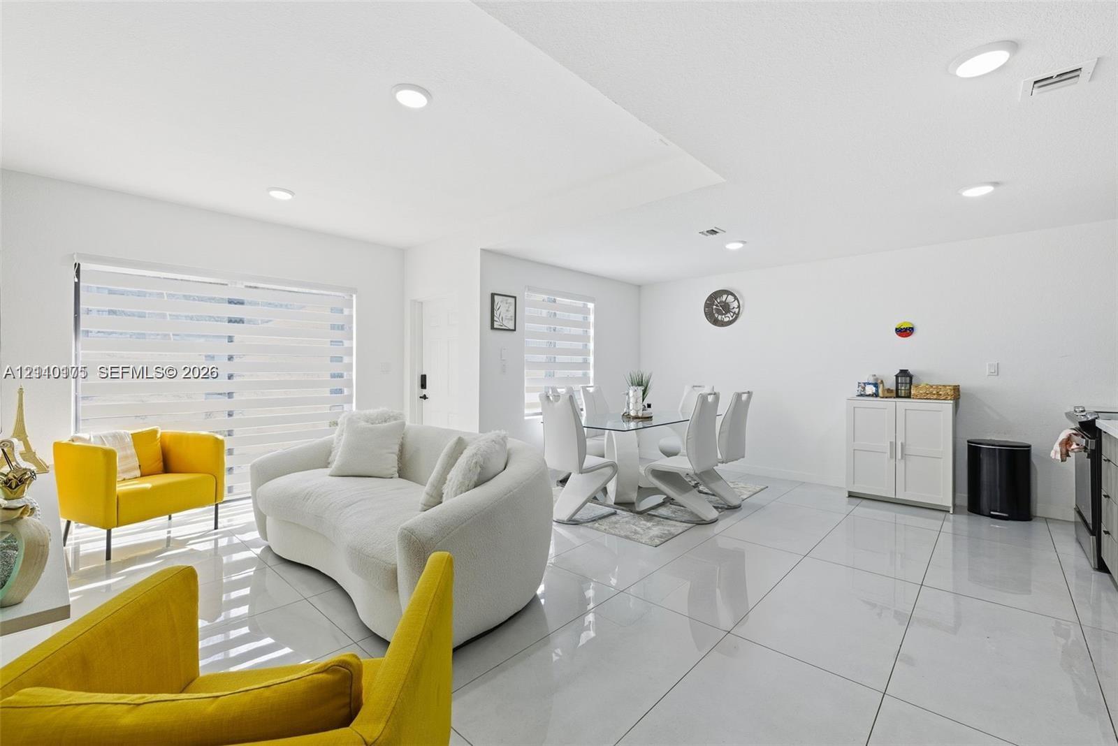 Open-concept interior featuring large-format ceramic tile flooring, recessed lighting, and expansive glass sliding doors with integrated horizontal window treatments