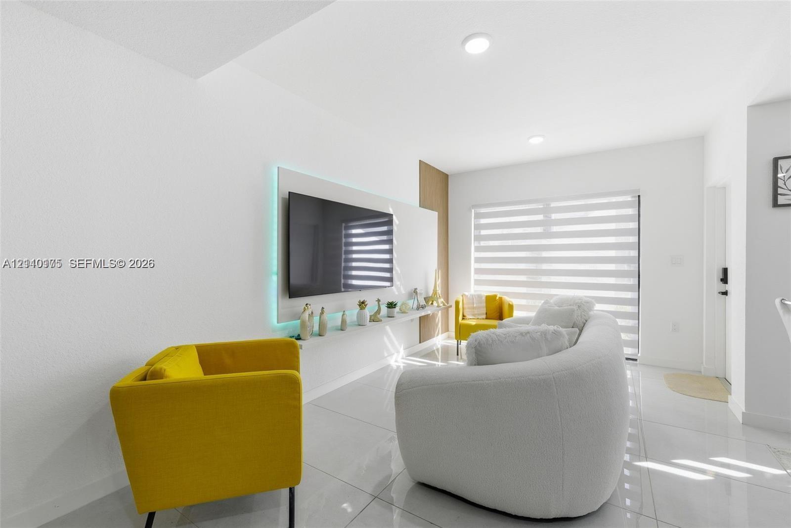 Large-format porcelain tile flooring, built-in media wall with recessed accent lighting, floor-to-ceiling wooden wall paneling, and adjustable horizontal window shades