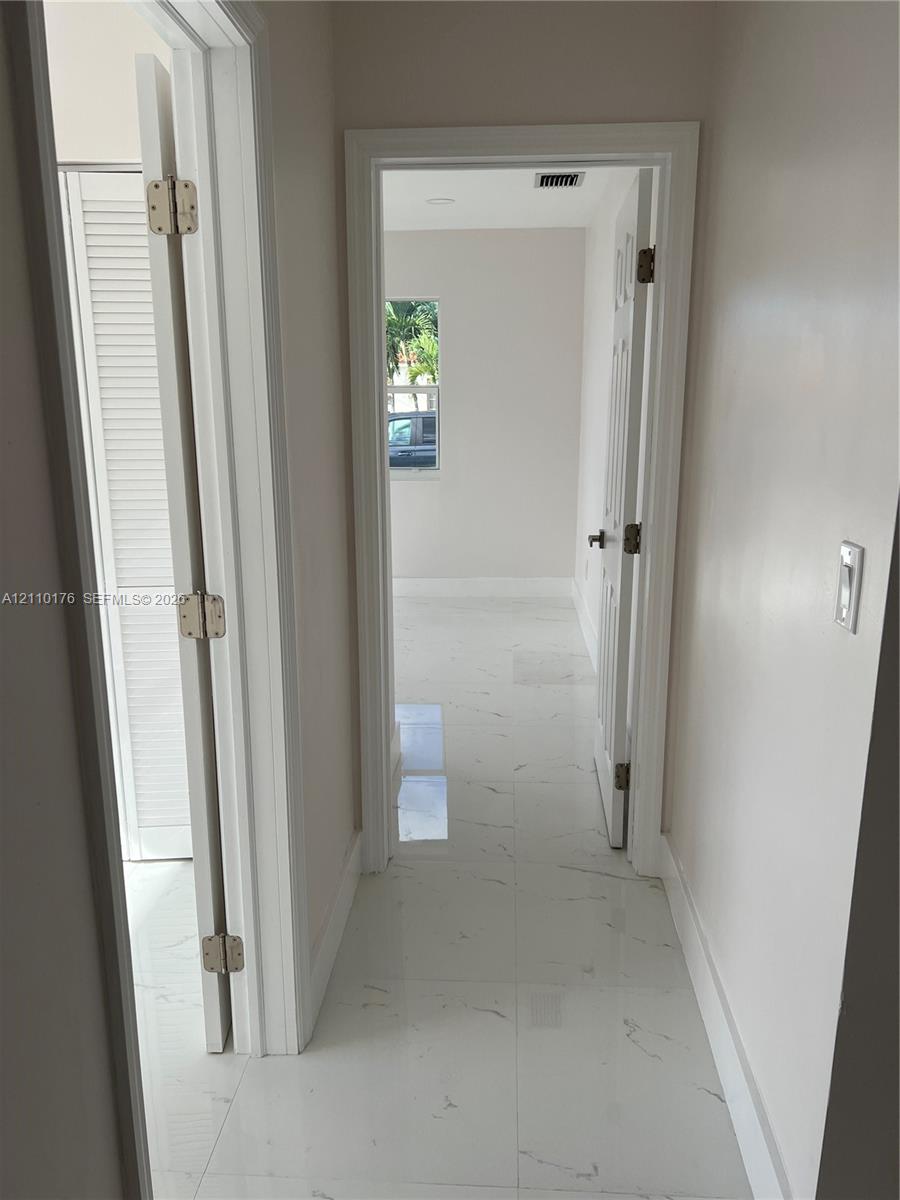 Hallway featuring light-colored stone-finish tile flooring, white interior doors with brushed metal hardware, and louvered closet doors