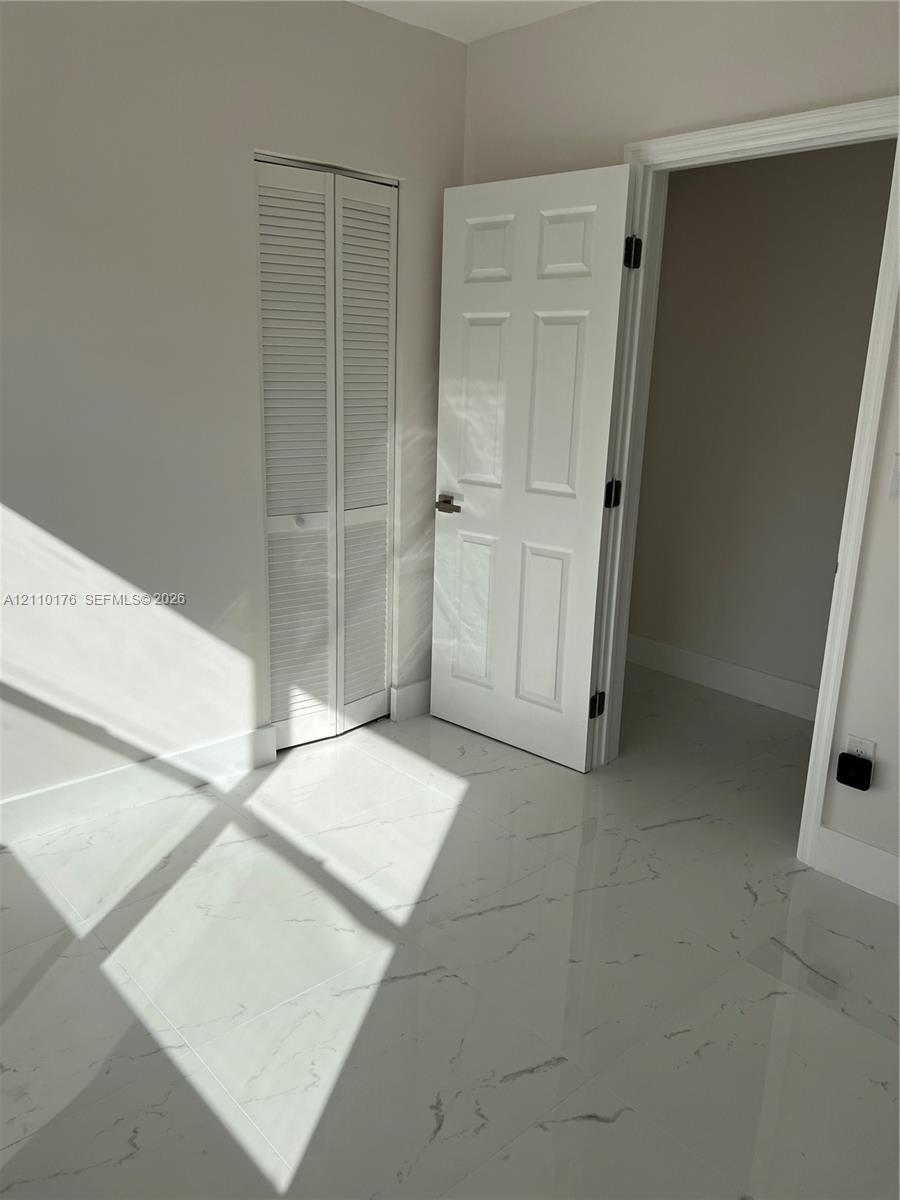 Polished stone-finish flooring with veining detail, white six-panel interior door with matte black hardware, and floor-to-ceiling white louvered closet doors