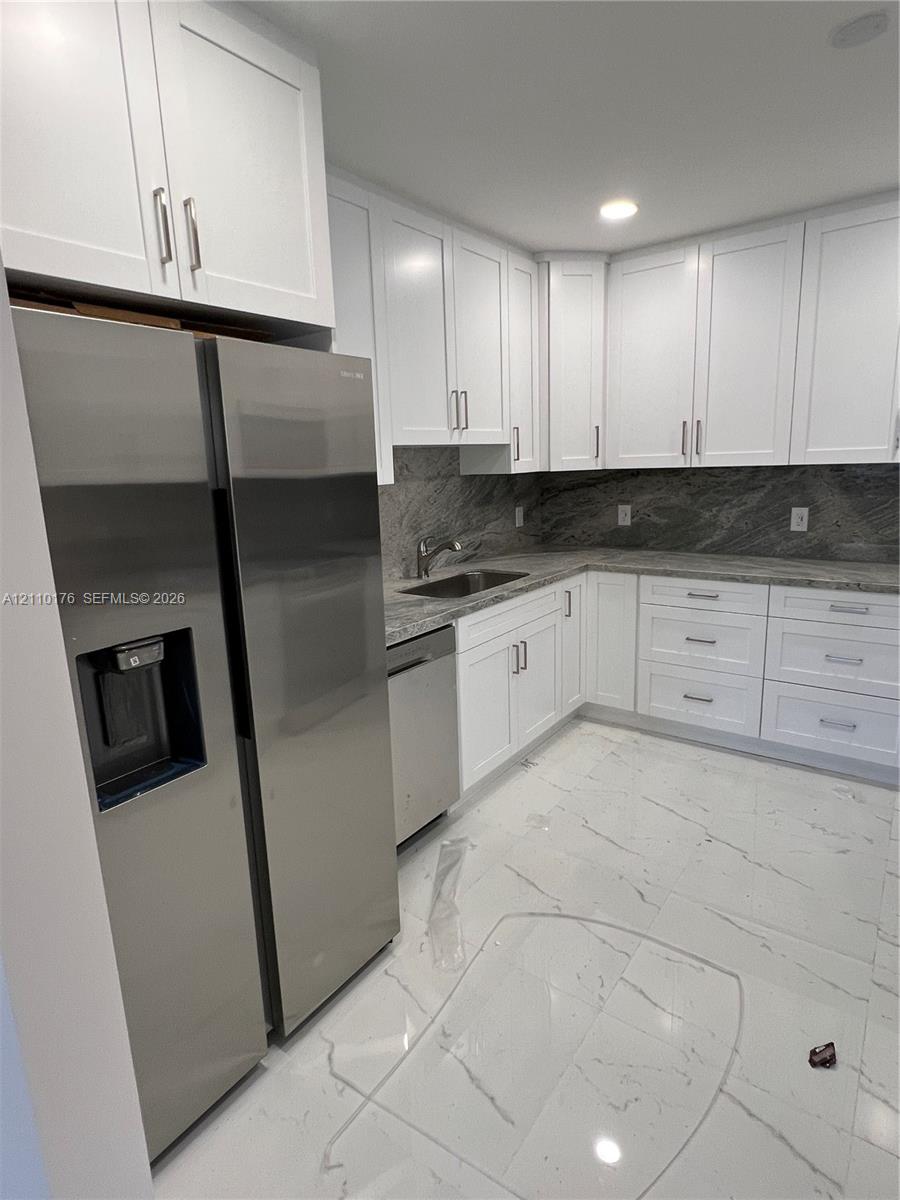 Kitchen featuring white shaker-style cabinetry, stainless steel appliances, stone countertops, stone tile backsplash, and polished stone-finish flooring