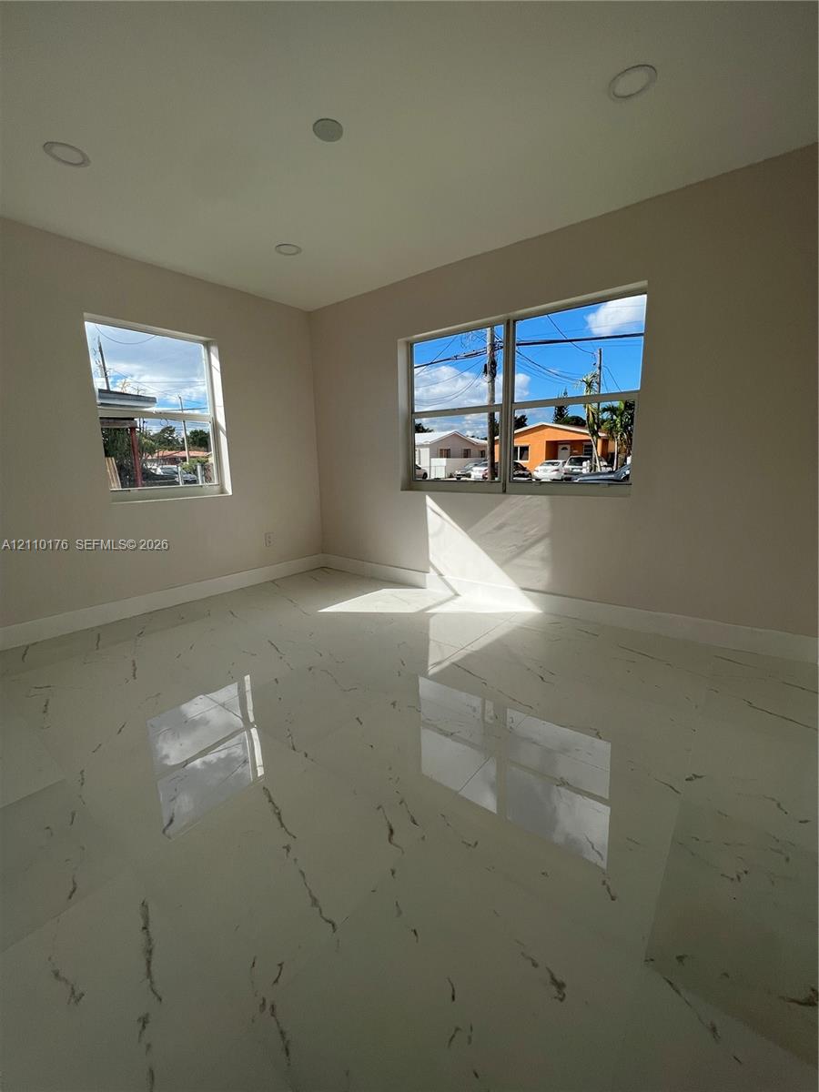 Neutral-toned interior space featuring polished large-format tile flooring with veining, recessed ceiling lighting, and dual aluminum-frame windows