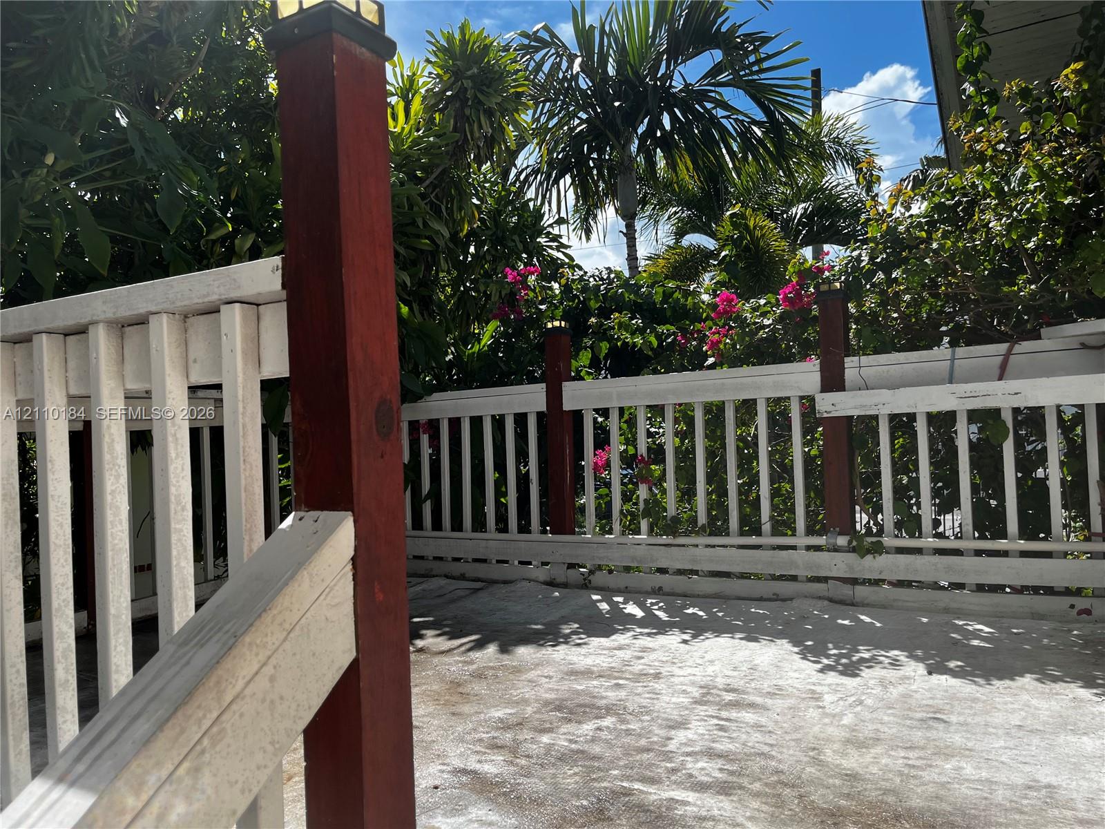 Outdoor deck with a concrete surface, white painted wood railing, integrated post lighting, and mature perimeter landscaping