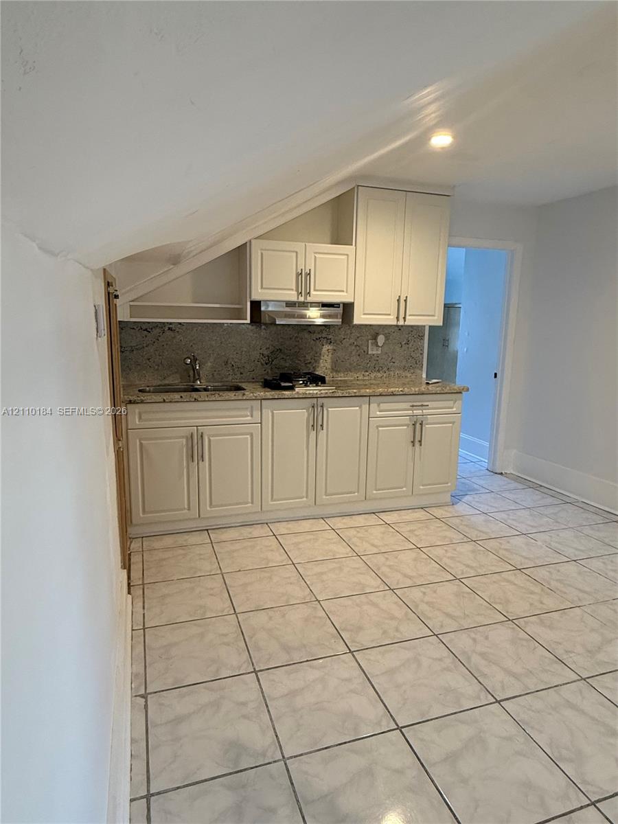 Kitchen featuring white shaker-style cabinetry, stone-finish countertops, stainless steel sink, gas cooktop, and tile flooring Kitchen featuring white shaker-style cabinetry, stone-finish countertops, stainless steel sink, gas cooktop, and tile flooring