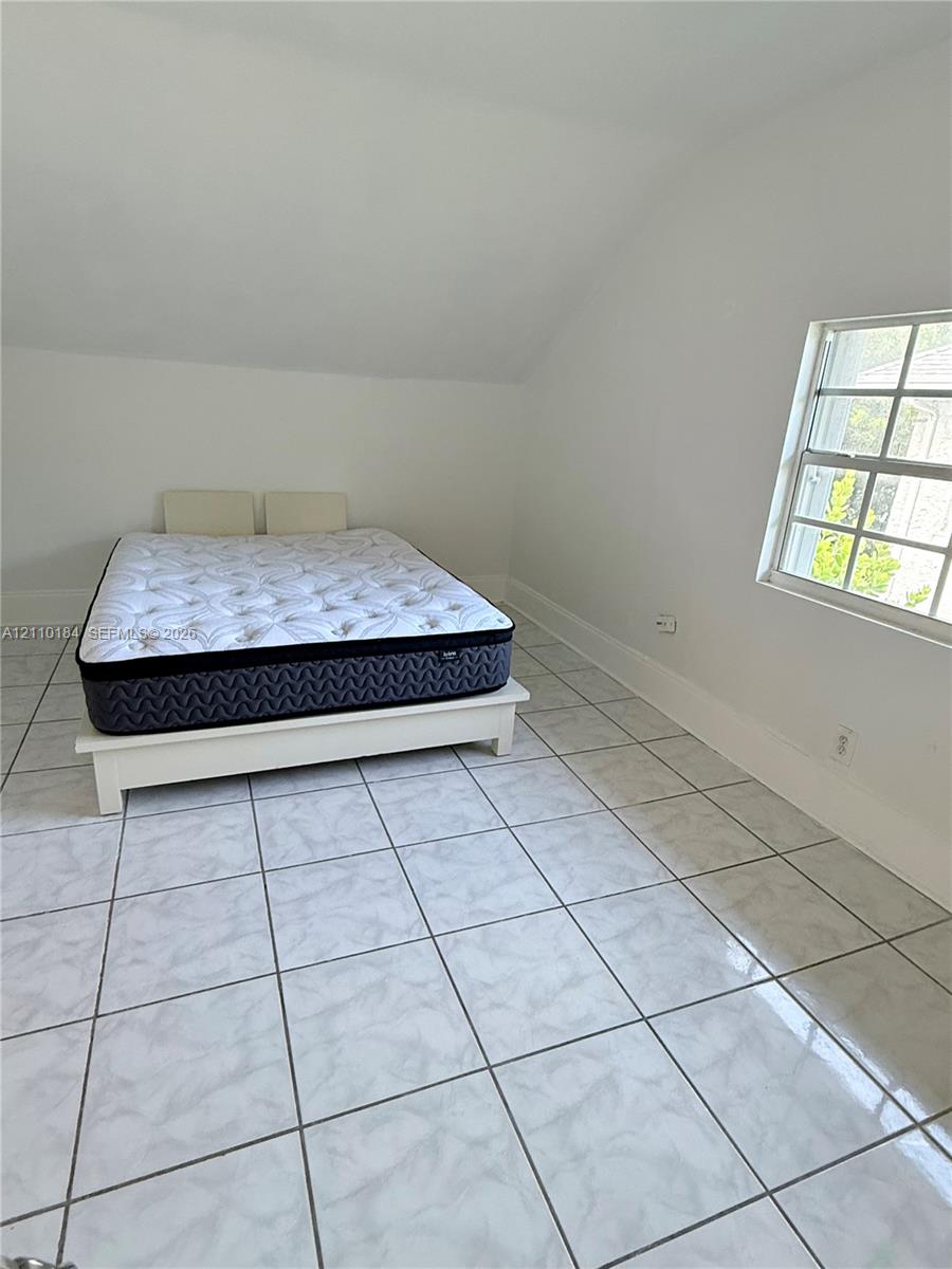 Light-filled room featuring white-toned tile flooring, angled ceiling, and a multi-pane grid window Light-filled room featuring white-toned tile flooring, angled ceiling, and a multi-pane grid window