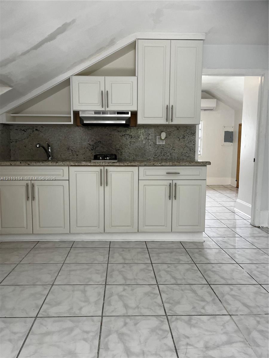 Kitchen featuring white shaker-style cabinetry, stone-finish countertops, tile flooring, and a stainless steel range hood Kitchen featuring white shaker-style cabinetry, stone-finish countertops, tile flooring, and a stainless steel range hood
