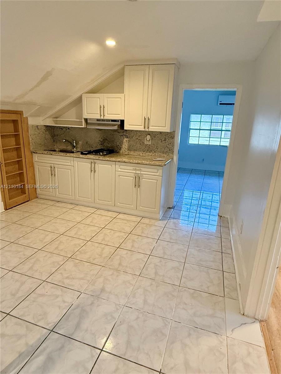 Kitchen area featuring shaker-style white cabinetry, stone-finish countertops, tile flooring, and integrated built-in shelving Kitchen area featuring shaker-style white cabinetry, stone-finish countertops, tile flooring, and integrated built-in shelving