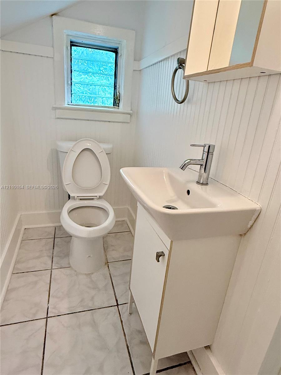 Bathroom featuring beadboard wall paneling, tile flooring, pedestal sink with a chrome faucet, and a wall-mounted medicine cabinet Bathroom featuring beadboard wall paneling, tile flooring, pedestal sink with a chrome faucet, and a wall-mounted medicine cabinet