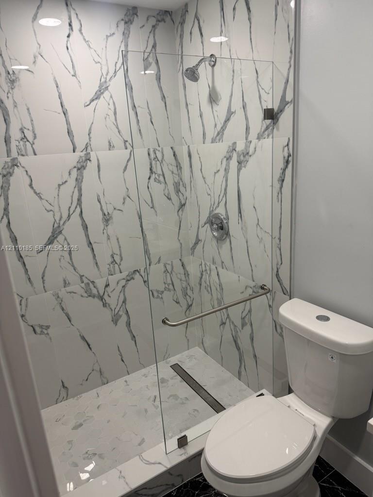 Walk-in shower featuring floor-to-ceiling veined tile, frameless glass enclosure, polished metal hardware, and linear drain