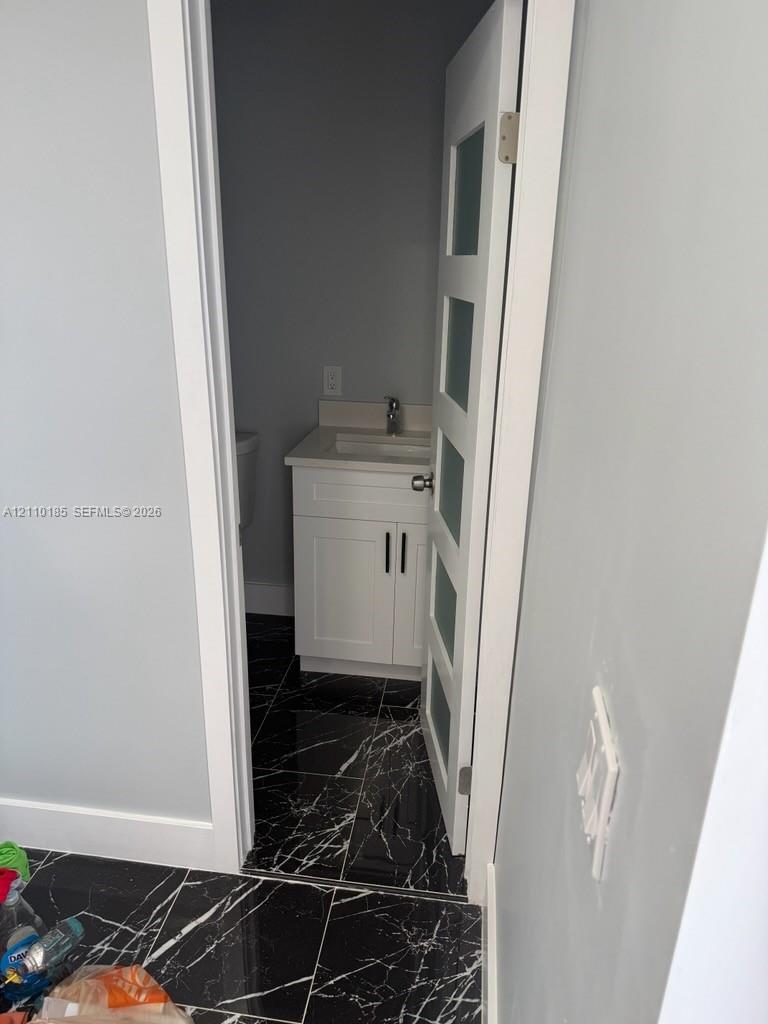 Interior space featuring high-contrast black veined tile flooring, a white vanity cabinet with shaker-style doors, and a door paneled with frosted glass inserts