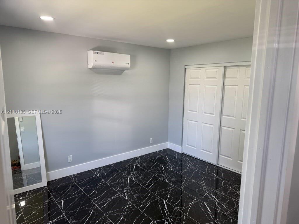 Interior space featuring high-gloss dark stone-finish tile flooring, a wall-mounted ductless mini-split climate control system, recessed ceiling lighting, and a white sliding-panel closet Interior space featuring high-gloss dark stone-finish tile flooring, a wall-mounted ductless mini-split climate control system, recessed ceiling lighting, and a white sliding-panel closet