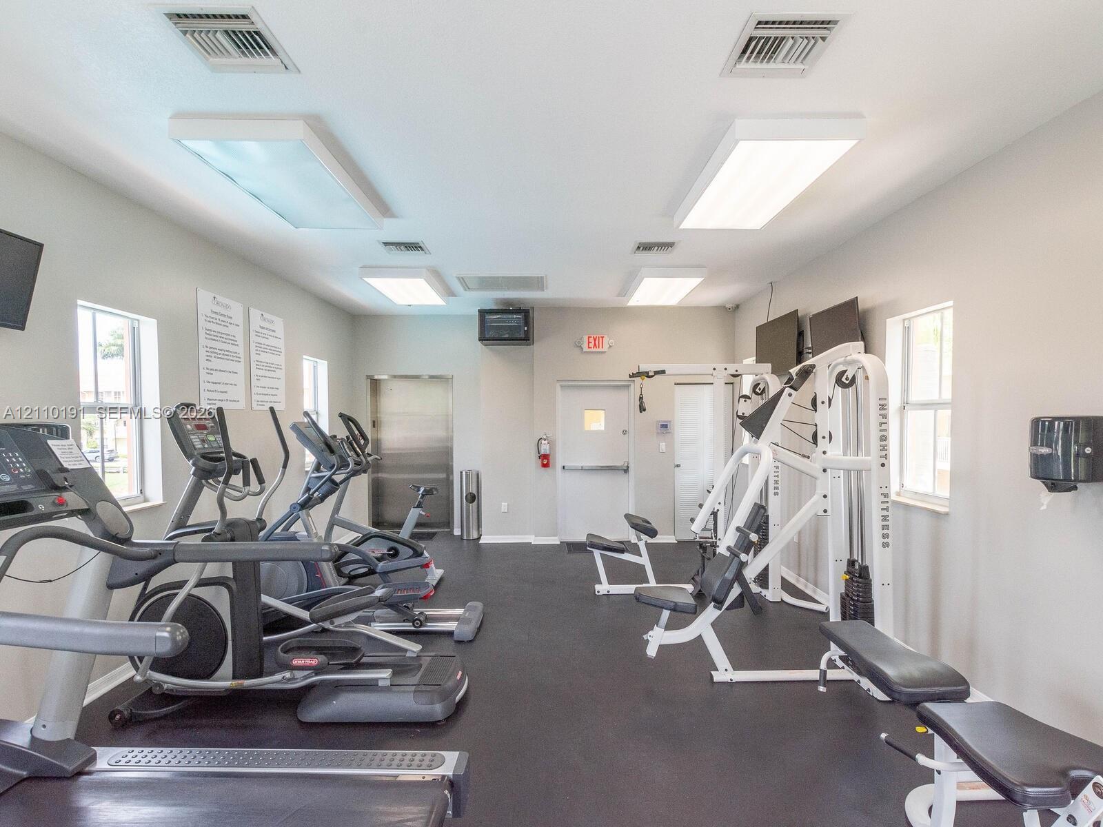 Fitness center featuring rubberized flooring, multiple windows providing natural light, and high-intensity overhead lighting