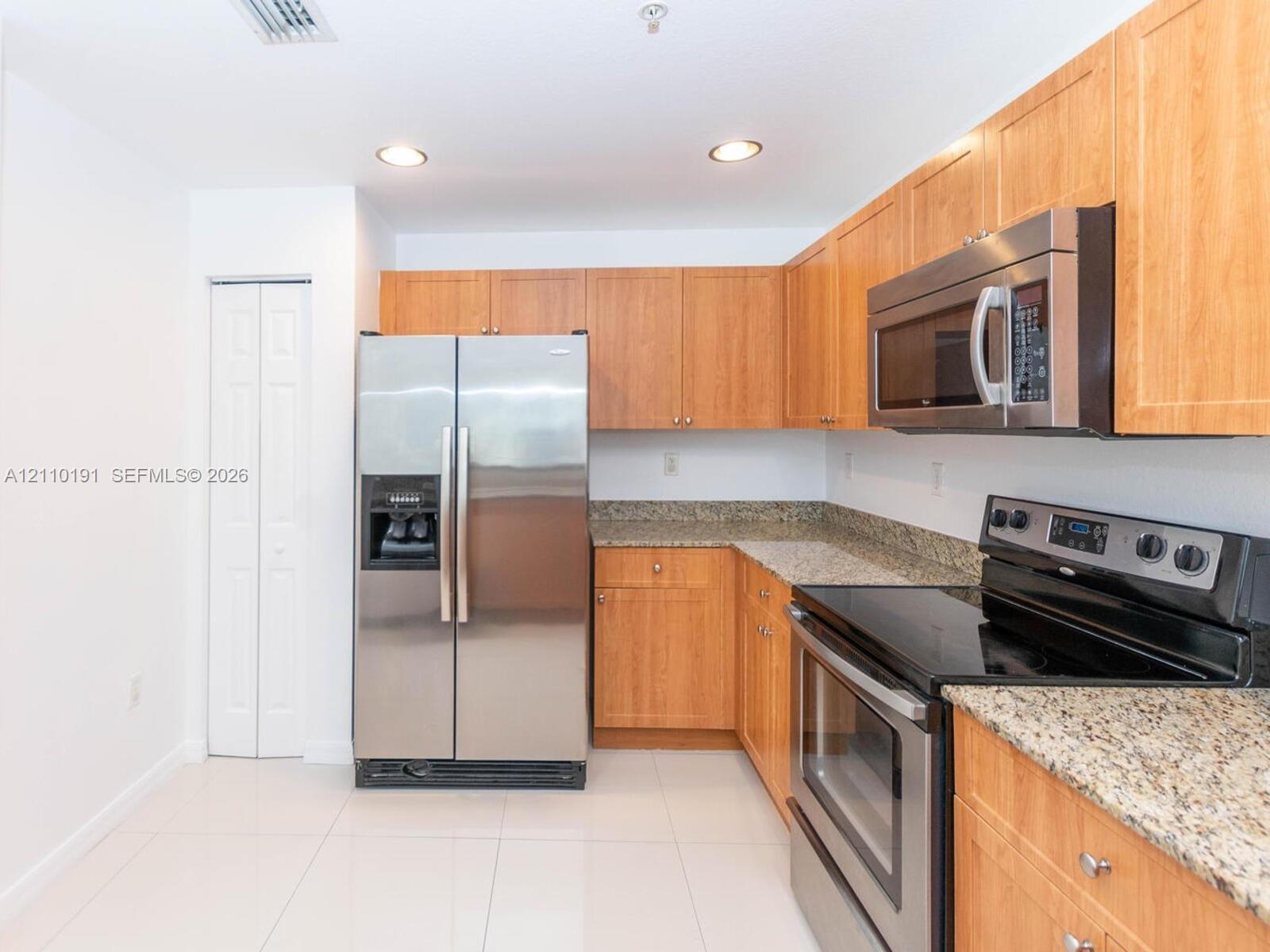 Kitchen featuring wood cabinetry, stone countertops, stainless steel appliances, and tile flooring