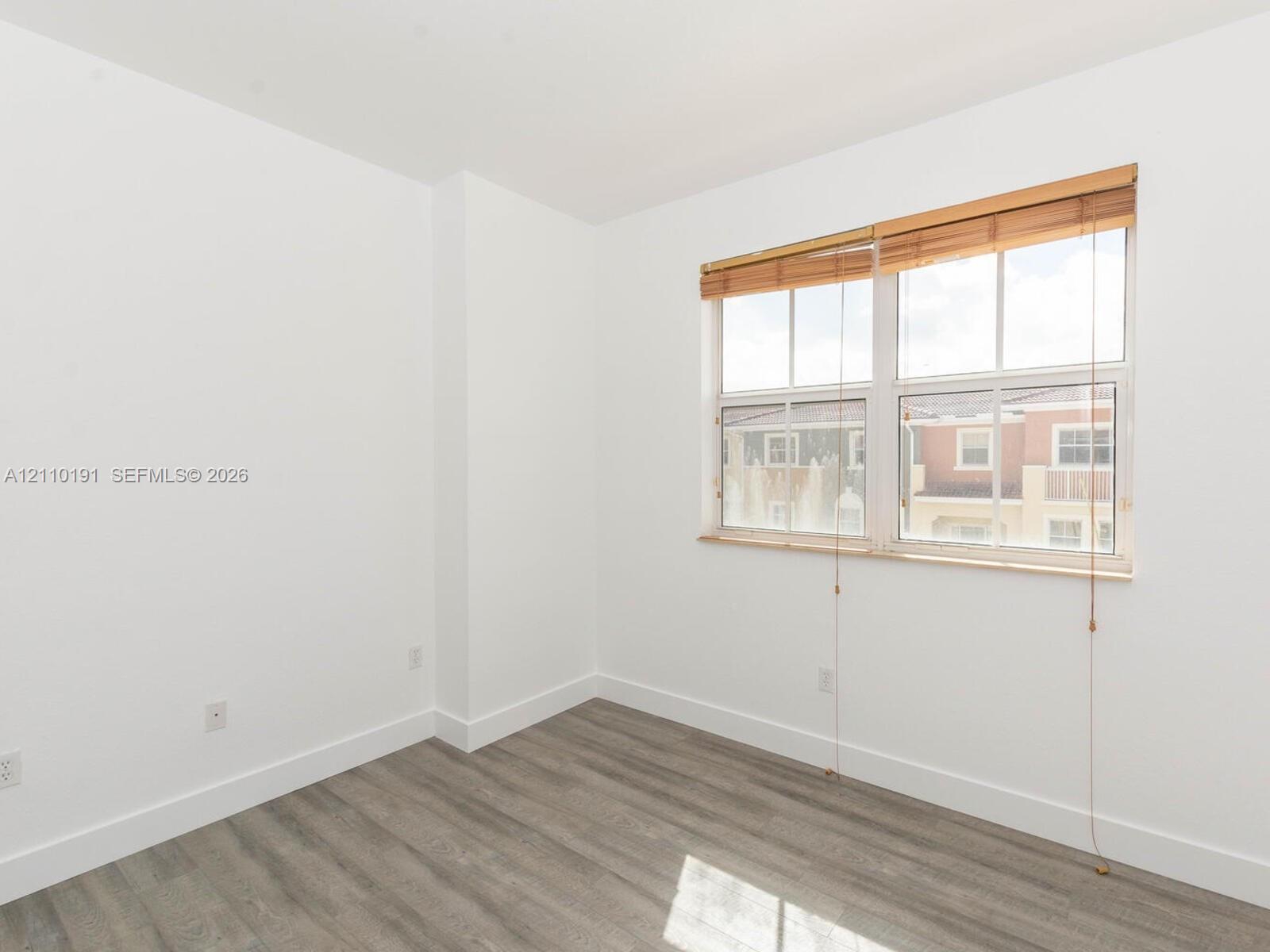 Neutral-toned walls paired with wood-finish flooring and a multi-pane window featuring installed wood blinds