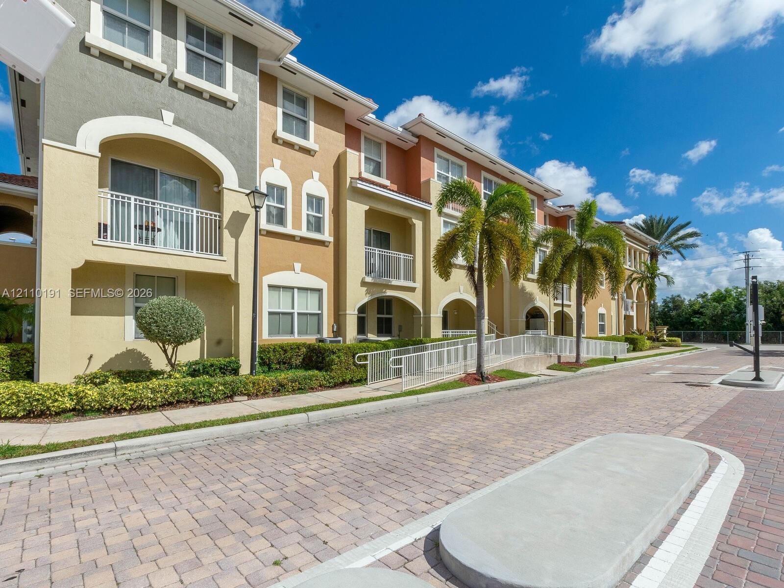Multi-story exterior featuring a stucco facade, arched architectural details, private balconies with metal railings, and unit-specific concrete ramps