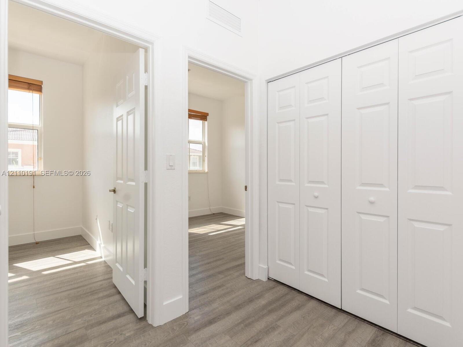 Hallway featuring wood-finish flooring, two sets of white paneled bifold closet doors, and interior paneled doors