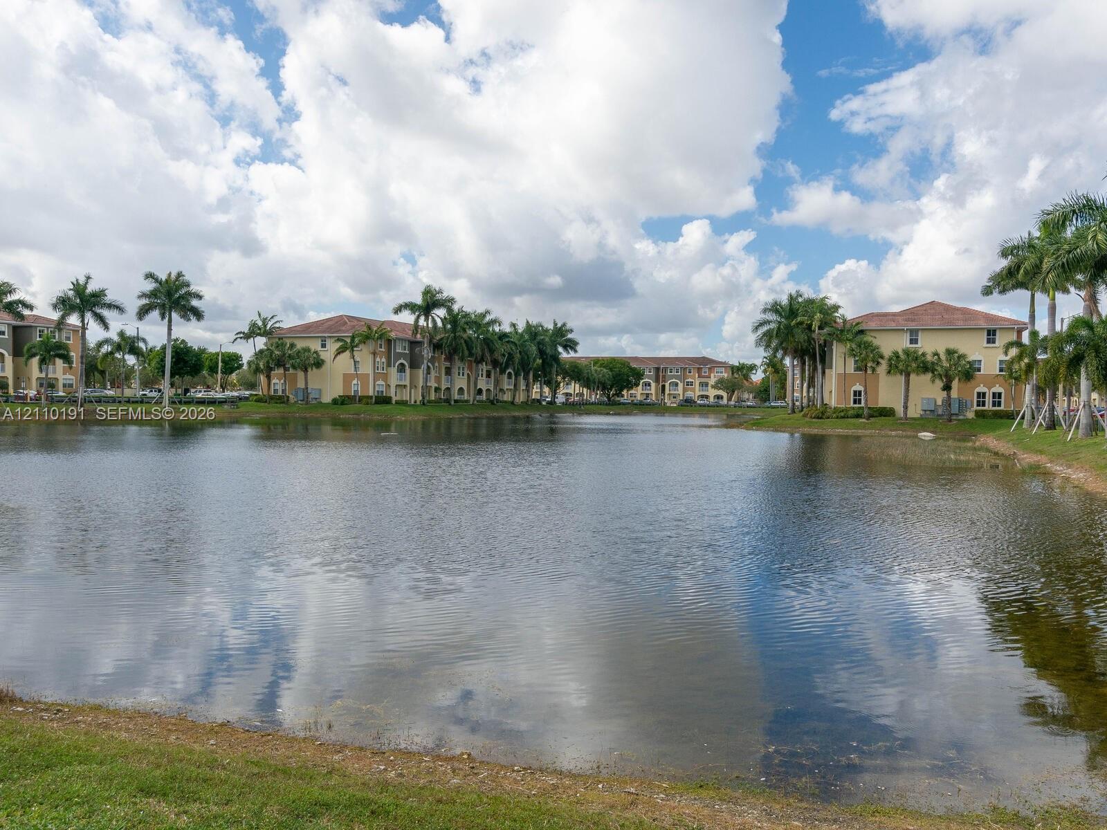 Waterfront location featuring a central pond, multi-story Mediterranean-style architecture, tile roofing, and perimeter landscaping with mature palm trees