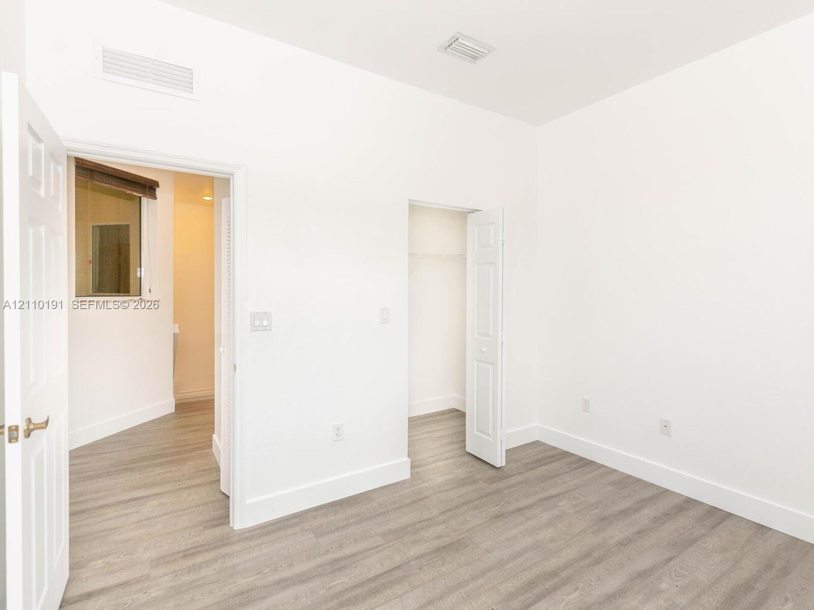 Interior space with wood-finish flooring, white walls, and a walk-in closet featuring built-in wire shelving